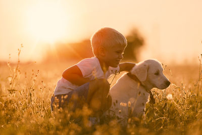 Boy with dog on field during sunset