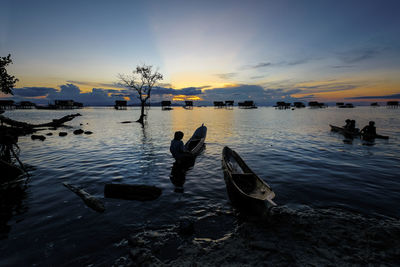 Silhouette boys in boat on sea against sky during sunset