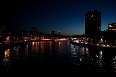River by illuminated buildings against clear sky at night