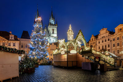 Illuminated christmas tree by building at night