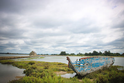 Scenic view of sea, old boat and watermill against sky