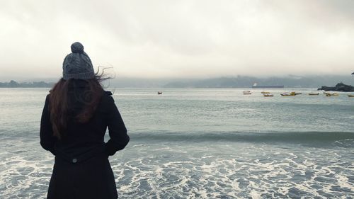 Rear view of woman standing by sea against sky during foggy weather