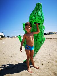 Full length of shirtless boy holding inflatable raft on beach