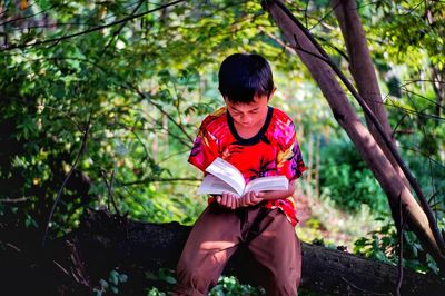 Full length of teenage girl sitting on book in forest
