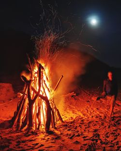 Woman walking on sand by fire at night