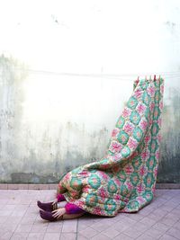 Woman covered in blanket sitting against wall