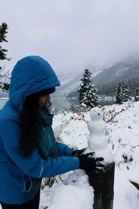 Woman making snowman on wooden post against lake and mountains