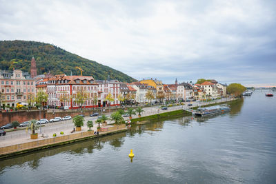 Houses by river and buildings in town against sky