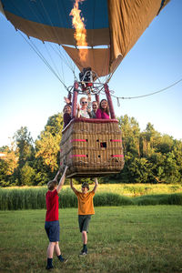 Low angle view of friends flying in hot air balloon while boys standing on grassy field