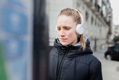 Young woman listening to music using parking meter in city