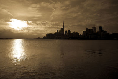 Silhouette buildings by sea against sky during sunset