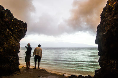 Rear view of friends standing on rock by sea against sky