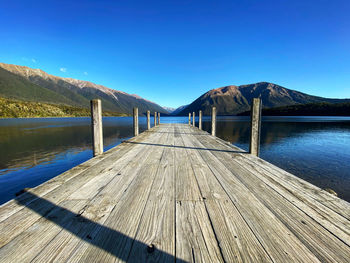 Wooden pier on lake against clear blue sky