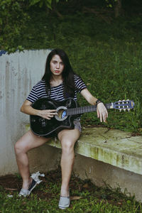 Portrait of young woman with guitar sitting outdoors