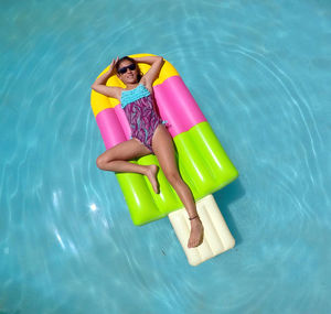 High angle view of young woman relaxing on pool raft in swimming pool during sunny day