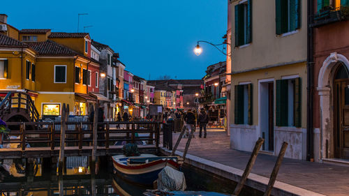 People on illuminated street amidst buildings in city at dusk