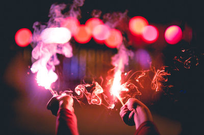 Cropped hands of child holding illuminated sparklers at night