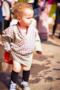 Cute child scratching on thigh while standing outdoors during sunny day