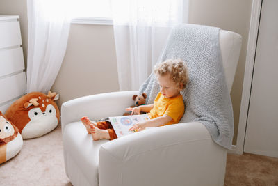 Boy toddler 2 years old sitting in armchair reading book. early age kid child development education