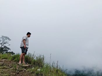 Full length of man standing on cliff against sky during foggy weather