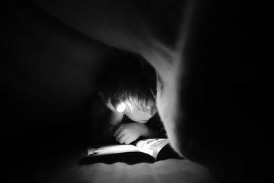 Boy with illuminated flashlight reading book in darkroom