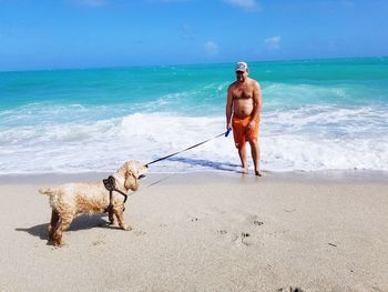 Shirtless man standing with dog at beach