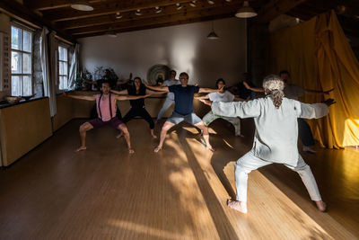 Full body back view of mature male instructor demonstrating technique of chi kung exercise for group of people during practice in studio