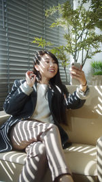 Portrait of smiling young woman holding camera while sitting outdoors