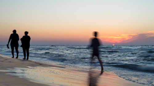 Silhouette people at beach against sky during sunset