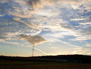 Electricity pylon on field against sky at sunset