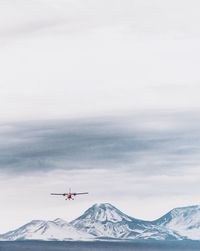 Helicopter flying over lake against snowcapped mountains