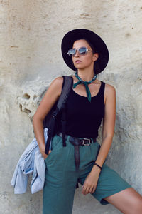 Woman traveler with a backpack and a hat stands next to a rock cave in the crimea in the summer