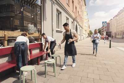 Female and male coworkers arranging bench outside cafe on sunny day