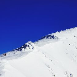 Low angle view of snowcapped mountains against clear blue sky on sunny day