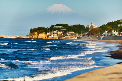 Scenic view of beach and snowcapped mountains against clear blue sky in the morning