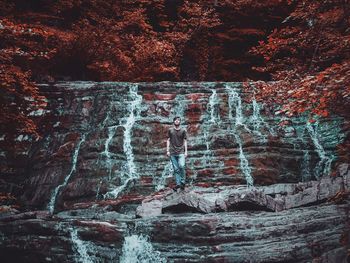 Young man standing at waterfall in forest