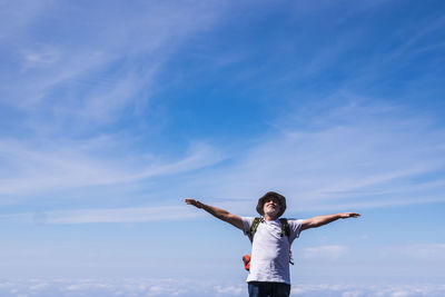 Man with arms outstretched standing against sky