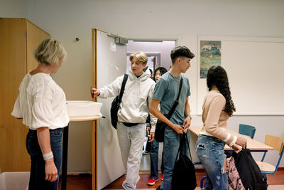 Teenage boy keeping smart phone in container on table while walking in classroom