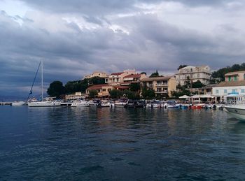 Sailboats in sea by buildings against sky