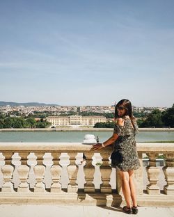 Young woman standing by railing against city