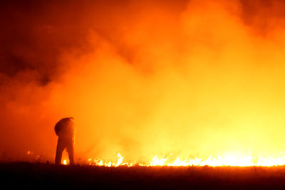 Rear view of firefighter standing on field against fire