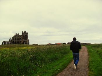 Rear view of woman walking on field against cloudy sky