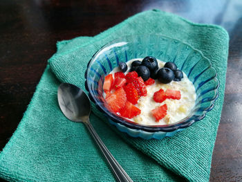 Cooked oat with forest fruits. strawberries and blueberries in a blue glass bowl on a green napkin.