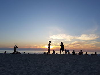 Silhouette people on beach against sky during sunset