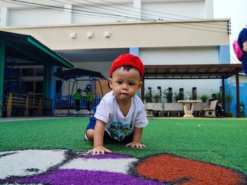 Portrait of cute boy crawling at lawn against buildings in city