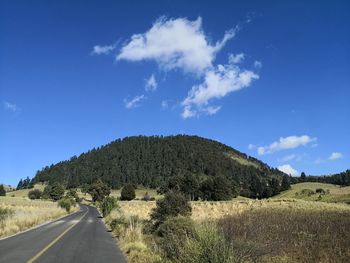 Empty road along countryside landscape against blue sky