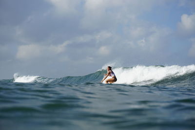 Side view of woman surfing in sea against sky