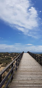 Boardwalk on footbridge against sky