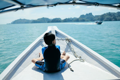 Rear view of boy sitting on boat in sea