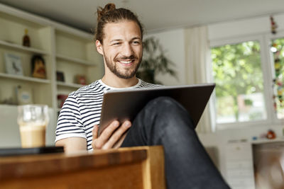 Young man with a bun sitting at home, using digital tablet